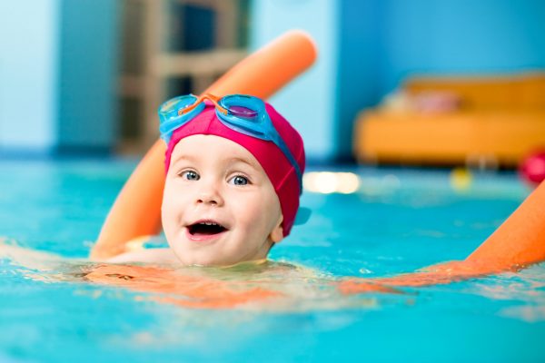 Happy little girl learning to swim with pool noodle